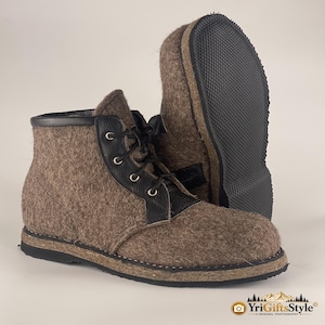 Könnte beinhalten: Ein Paar knöchelhohe Stiefel aus braunem Filz mit schwarzen Lederschnürungen, silbernen Metallösen und schwarzen Schnürsenkeln. Die Stiefel haben eine schwarze, strukturierte Gummisohle sowie einen schwarzen Lederbesatz am oberen Rand.