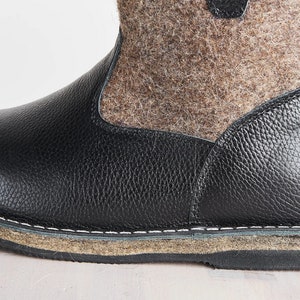 Puede incluir: Primer plano de una bota de cuero negro con una parte superior de fieltro marr&oacute;n. La bota tiene una costura cosida alrededor de la suela y una suela gruesa y texturizada.