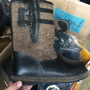 Puede incluir: Botas de fieltro marr&oacute;n y negro con parte superior de cuero negro y suela de goma gruesa. Las botas tienen dos hebillas negras en el lateral.