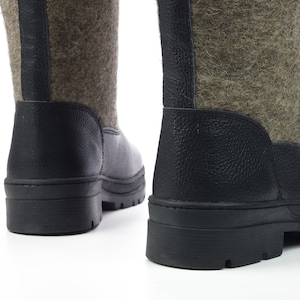 Puede incluir: Un par de botas de media ca&ntilde;a con una parte superior de fieltro verde oliva texturizado y adornos negros de aspecto cuero. Las botas tienen una suela gruesa de goma negra con tacos y una tira vertical negra detr&aacute;s.