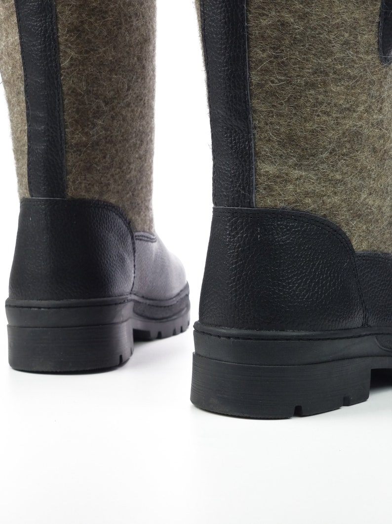 Puede incluir: Un par de botas de media ca&ntilde;a con una parte superior de fieltro verde oliva texturizado y adornos negros de aspecto cuero. Las botas tienen una suela gruesa de goma negra con tacos y una tira vertical negra detr&aacute;s.