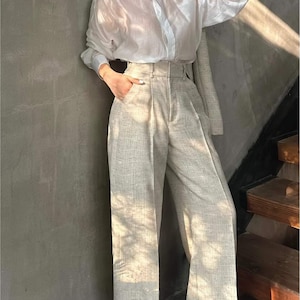 May include: A woman wearing a white sheer button-down shirt and beige wide-leg pants with a high waist.