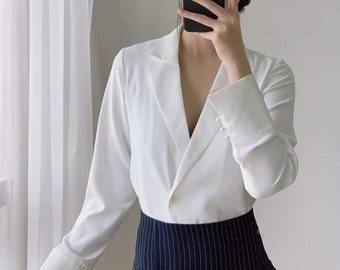 May include: A white long-sleeve blazer with a notched lapel and pearl button details on the cuffs. The blazer is paired with a navy blue pinstripe skirt with two decorative buttons.