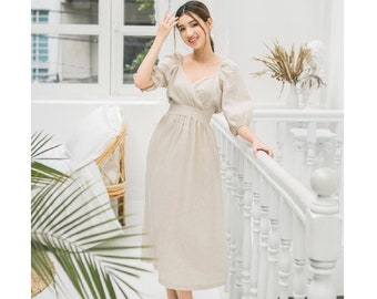 May include: A woman wearing a beige linen dress with a V-neckline and puff sleeves. She is standing on a white staircase with a white railing.