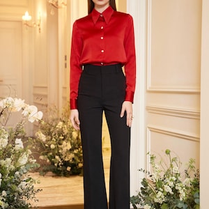 May include: A red long-sleeve button-down shirt paired with black flared trousers. The shirt has a classic collar and buttoned cuffs. The high-waisted trousers have a wide leg. The outfit is suitable for formal or business attire.