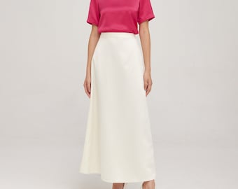 May include: A woman wearing a bright pink satin top with short sleeves and a white maxi skirt. She is wearing white heels.
