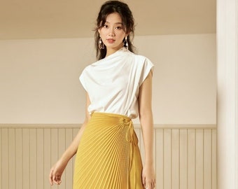 May include: A woman wearing a white top and a yellow pleated skirt. She is holding a white handbag.