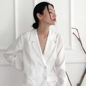 Puede incluir: Una chaqueta blanca con cierre de doble botonadura y mangas largas. La chaqueta est&aacute; hecha de una tela suave y ligera.