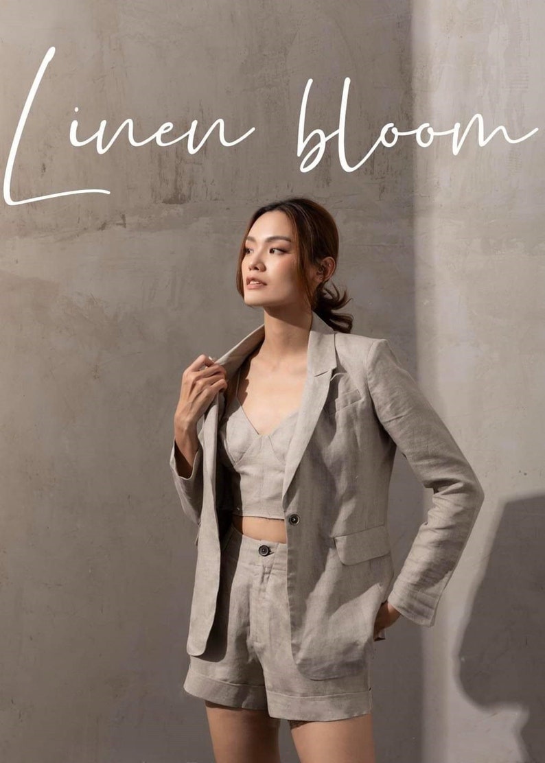 May include: A woman wearing a light grey linen blazer, matching linen shorts, and a linen crop top. The text "linen bloom" is written in white script at the top of the image.