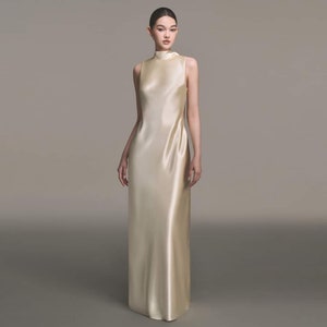 Puede incluir: Un vestido de sat&eacute;n marfil sin mangas, con cuello alto y silueta ajustada. El vestido tiene un dise&ntilde;o simple y elegante, perfecto para una ocasi&oacute;n formal.