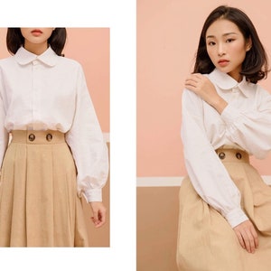 May include: A white collared blouse with long sleeves and a brown pleated skirt. The blouse has a Peter Pan collar and the skirt has a high waist.