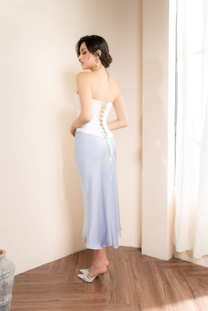 May include: A white corset top with a lace-up back is paired with a light blue, floor-length skirt. The outfit is completed with light blue heels. The ensemble is elegant and suitable for formal occasions.
