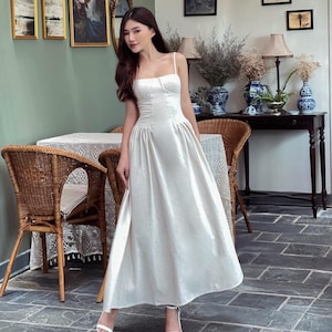 May include: A white sleeveless maxi dress with a fitted bodice and a flowing skirt. The dress has a simple, elegant design and is perfect for a variety of occasions.