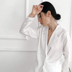 Puede incluir: Una chaqueta blanca con cierre de doble botonadura y mangas largas. La chaqueta est&aacute; hecha de una tela suave y ligera.