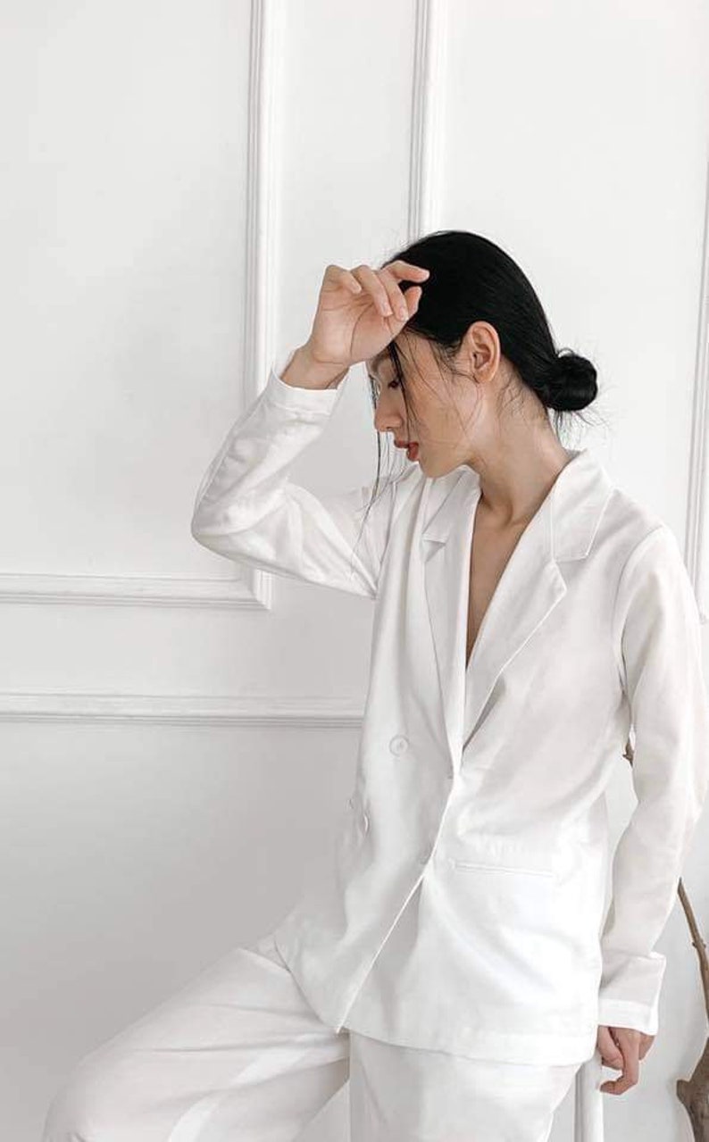 Puede incluir: Una chaqueta blanca con cierre de doble botonadura y mangas largas. La chaqueta est&aacute; hecha de una tela suave y ligera.