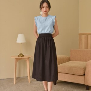 May include: A woman wearing a light blue sleeveless blouse with a black midi skirt and black lace-up shoes.