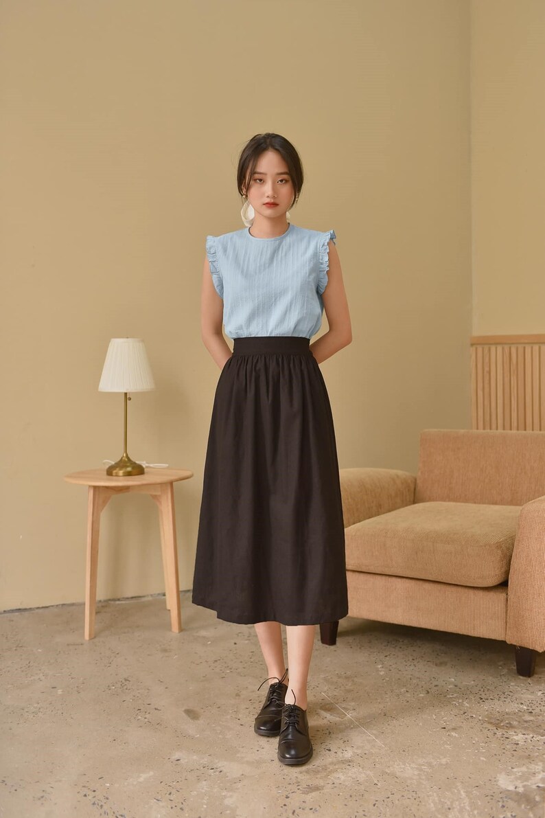 May include: A woman wearing a light blue sleeveless blouse with a black midi skirt and black lace-up shoes.