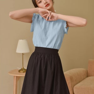 May include: A woman wearing a light blue, short-sleeved blouse with ruffled trim and a black, knee-length skirt.