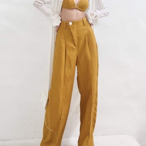 May include: A mustard yellow wide-leg linen pant with a high waist and pleats. The pant has a button closure and a relaxed fit.