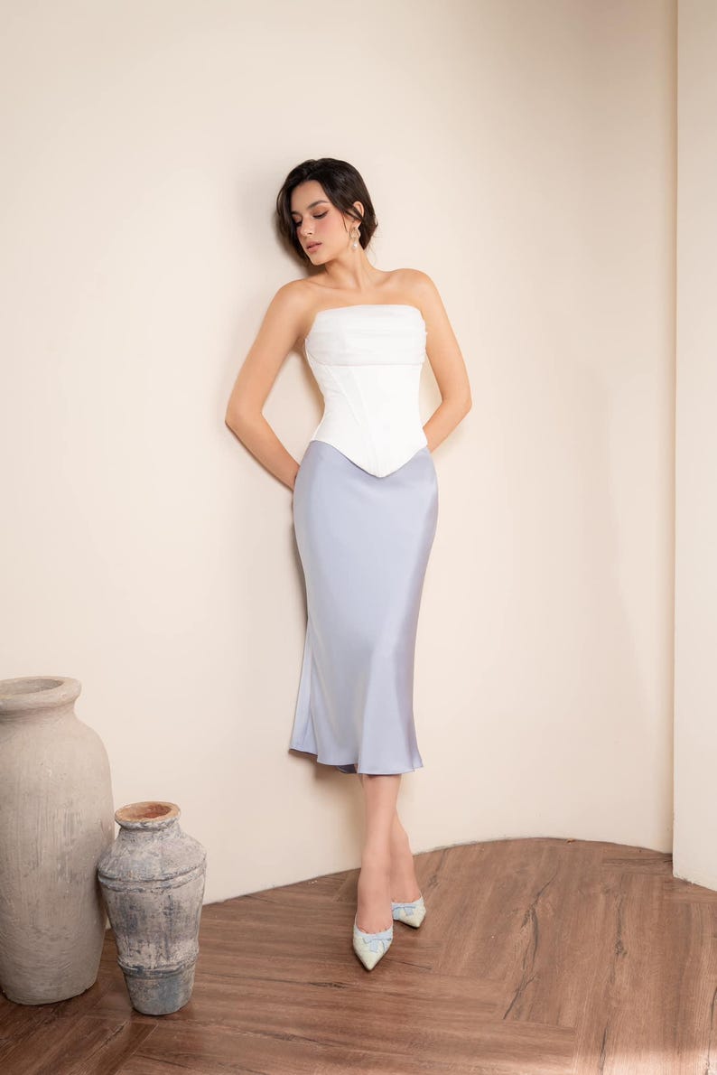 May include: A strapless white corset top paired with a light blue satin midi skirt. The outfit is completed with patterned heels. The ensemble is a formal wear outfit.