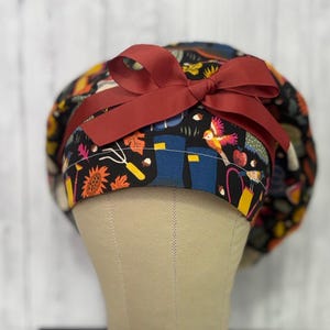 May include: A black gardening hat with a colorful print of birds, gardening tools, and autumn leaves. The hat has a burgundy bow on the front. The hat is on a mannequin head.
