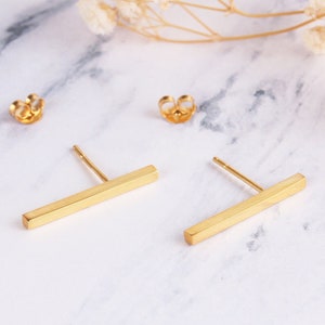 May include: A pair of gold bar earrings. The earrings are simple and minimalist, with a straight bar design.