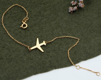May include: A gold chain bracelet with a small airplane charm. The bracelet is on a green fabric background.
