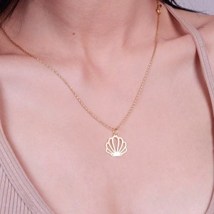 Op de afbeelding: Een gouden ketting met een delicate schelp hanger. De ketting wordt gedragen door een persoon met donker haar en een lichtgekleurde top.