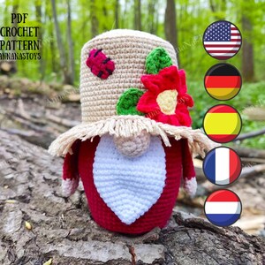 May include: Crocheted gnome with a red heart, wearing a straw hat with a ladybug and a red flower. The gnome is sitting on a tree trunk. The image includes flags of the United States, Germany, Spain, France, and the Netherlands.