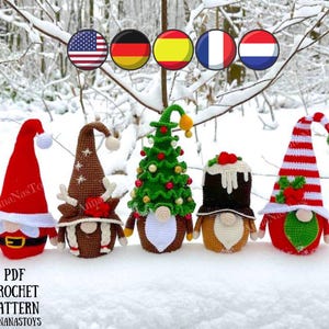 May include: Five crocheted Christmas gnomes in various designs, including a reindeer, a Christmas tree, a pudding, and two traditional gnomes. The gnomes are standing on a snowy surface.
