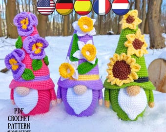 May include: Three crocheted gnomes with different flower designs on their hats. The gnome on the left has a purple and pink hat with purple pansies, the middle gnome has a purple hat with white and yellow daffodils, and the gnome on the right has a green hat with yellow sunflowers.