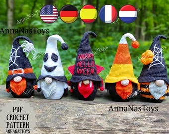 May include: Four crocheted Halloween gnomes with different designs. The gnomes are wearing hats with various Halloween themes, including a spider web, a ghost, a vampire, and a candy corn. The gnomes are sitting on a wooden surface.
