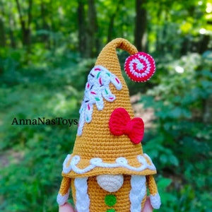 May include: A gingerbread gnome crochet doll with white icing, red and white candy, and green sprinkles. The gnome is wearing a red bow and has white yarn hair.