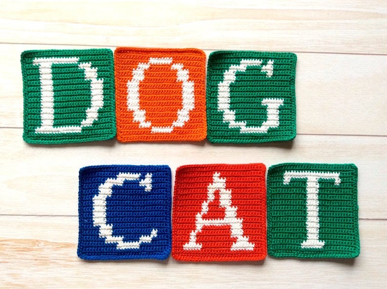 Może przedstawiać: Kwadraty na szydełku z wyhaftowanymi słowami "DOG CAT" białą nicią. Kwadraty są zielone, pomarańczowe, niebieskie i czerwone.