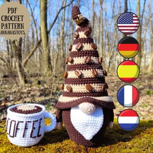 Puede incluir: Patrón de crochet para un gnomo de café con un sombrero a rayas marrón y beige, barba marrón y pecho en forma de corazón blanco. El gnomo sostiene una taza de café blanca con la palabra "COFFEE" escrita en ella. El patrón está disponible en inglés, alemán, español, francés y holandés.