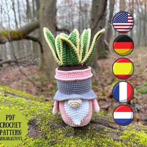 Op de afbeelding: Een gehaakte kabouterplanter met een groen-gele plant. De kabouter is roze, grijs en wit, met een lange witte baard. De tekst "PDF CROCHET PATTERN ANNANASTOYS" is zichtbaar.