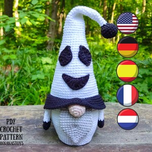 May include: A crochet ghost gnome pattern. The gnome is white with a black smiling face and a black hat. The gnome has a white beard. The pattern is available in multiple languages.