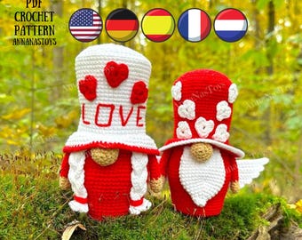 May include: Two crocheted gnomes, one wearing a white hat with the word "LOVE" on it and the other wearing a red hat with white hearts. Both gnomes are wearing red and white outfits and have white beards.