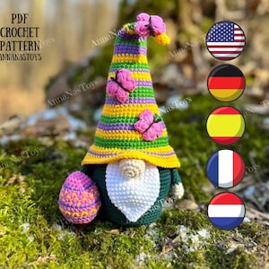 Può includere: Schema a uncinetto per un gnomo verde e giallo con un cappello a righe viola e giallo, che tiene un uovo di Pasqua rosa e viola. Lo gnomo ha una barba bianca e una farfalla rosa sul cappello. Lo schema è disponibile in formato PDF.