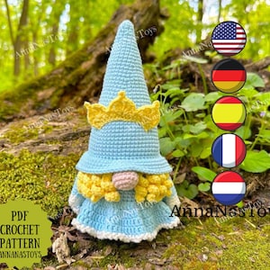 Könnte beinhalten: Eine gehäkelte Gnompuppe, die einen hellblauen Hut mit einer gelben Krone, einen gelben Bart und ein hellblaues Kleid trägt. Der Gnom sitzt auf einem Moosbett in einer Waldlandschaft. Das Bild zeigt auch die Flaggen der Vereinigten Staaten, Deutschlands, Spaniens, Frankreichs und der Niederlande.