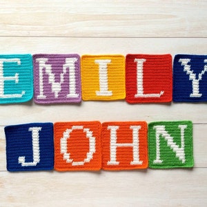 Może przedstawiać: Kwadraty na szydełku, kt&oacute;re tworzą imiona "Emily" i "John" białymi literami. Kwadraty są w r&oacute;żnych kolorach, w tym niebieskim, fioletowym, ż&oacute;łtym, czerwonym i zielonym.