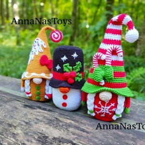 May include: Three crocheted Christmas gnomes, one gingerbread themed, one snowman themed, and one with a candy cane hat and green bow. The gnomes are sitting on a wooden surface with a green background. The text "AnnaNasToys" appears twice in the image.