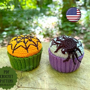 May include: Two crocheted Halloween cupcake amigurumi toys. One is orange with a black spiderweb design and a green base. The other is purple with a gray spiderweb design and a spider on top. The toys are on a wooden surface. PDF CROCHET PATTERN ANNANASTOYS