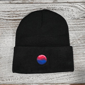 May include: Black beanie with a circular patch featuring a pink, red, and blue mountain design.
