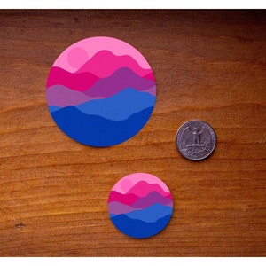 May include: Two round stickers with a layered mountain design in shades of pink, purple, and blue. The larger sticker is about the size of a US quarter.