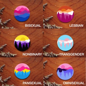 May include: A set of 12 round stickers featuring different pride flag designs with mountain and forest scenes. The stickers are arranged in a grid on a wooden surface. The text "Choose the stickers you would like and write them in personalizations!" is visible in the lower right corner of the image.