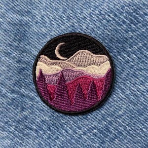 May include: Purple, pink, and white embroidered mountain range with a crescent moon in the sky. The design is on a black circle patch.