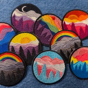 May include: Nine embroidered patches featuring colorful mountain landscapes with a rainbow, clouds, and a crescent moon. The patches are circular and have a black outline.