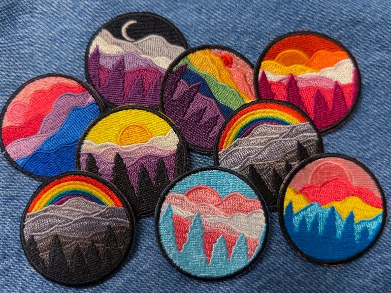 May include: Nine embroidered patches featuring colorful mountain landscapes with a rainbow, clouds, and a crescent moon. The patches are circular and have a black outline.