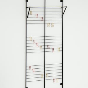 Könnte beinhalten: Ein schwarzer Wandorganizer aus Metall mit horizontalen Stangen und mehreren kleinen Haken in Rot und Gold. Der Organizer hat zwei abgewinkelte Stangen oben zum Aufhängen von Gegenständen.